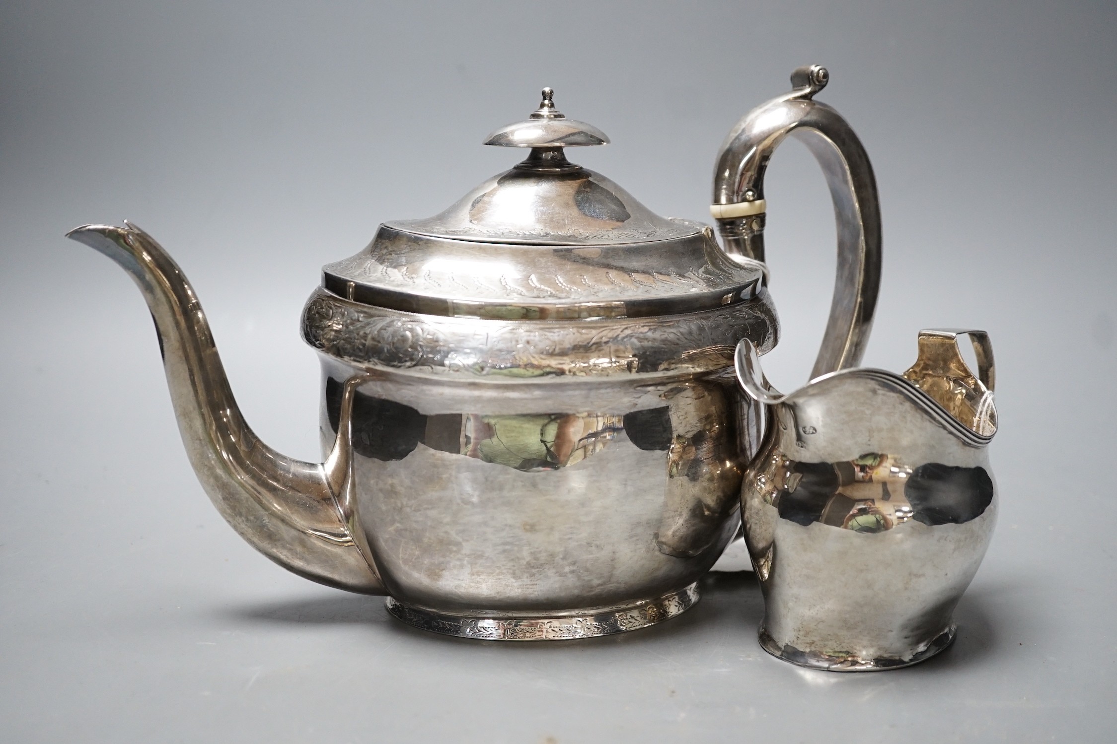 A George III engraved silver oval teapot on stand, Hannah Northcote? London, 1804 and Georgian silver cream jug, marks rubbed, gross 24.8oz.